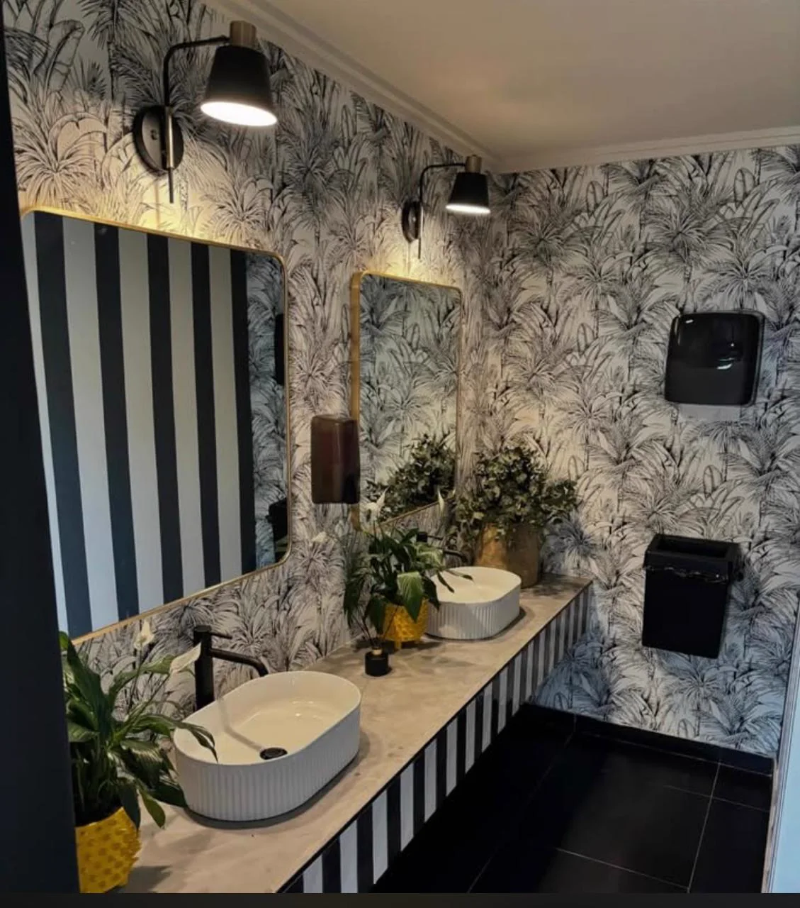 Statement bathroom with a striped double vanity, botanical wallpaper and black wall lights
