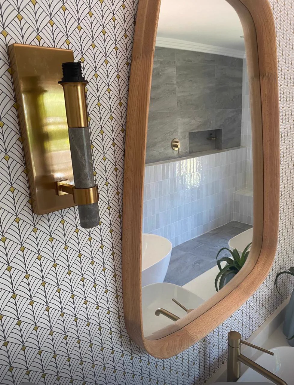 Rounded timber-framed bathroom mirror with a brass wall light and textured tiles