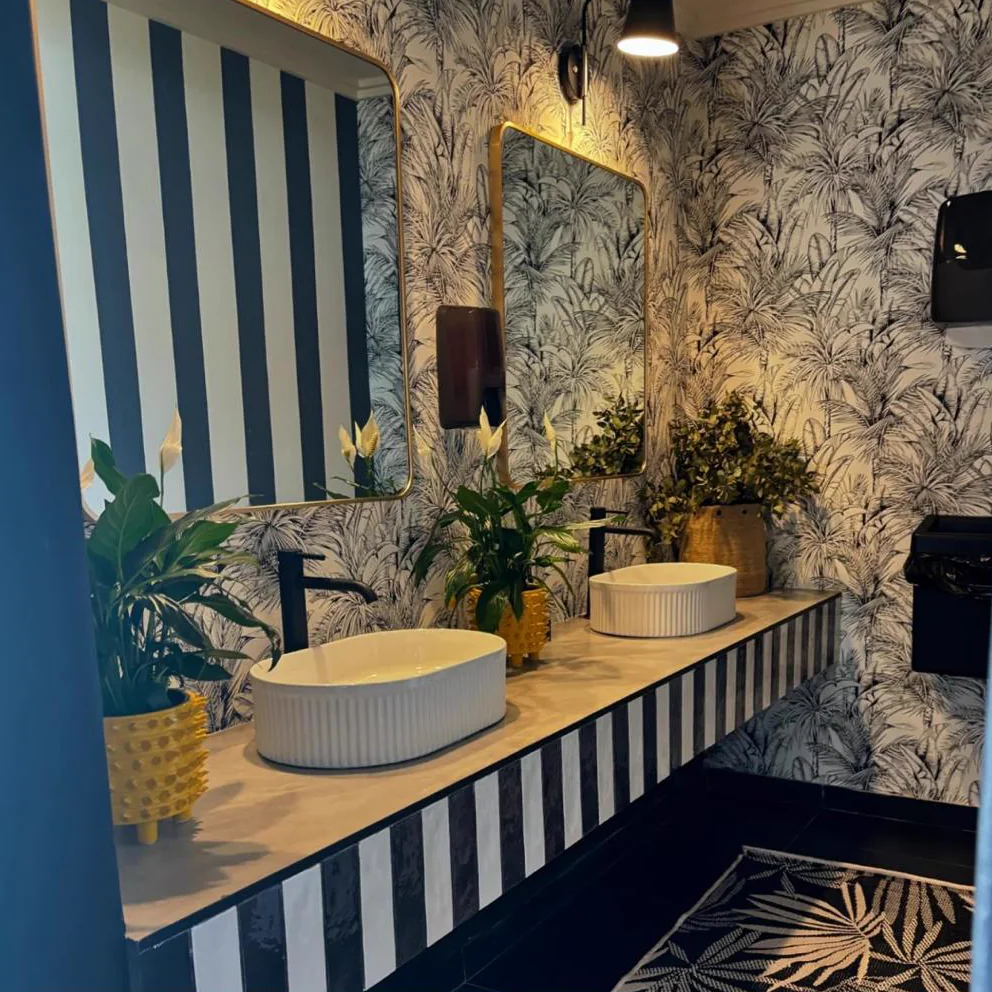 Bold bathroom vanity with striped cabinetry, botanical wallpaper and twin vessel basins