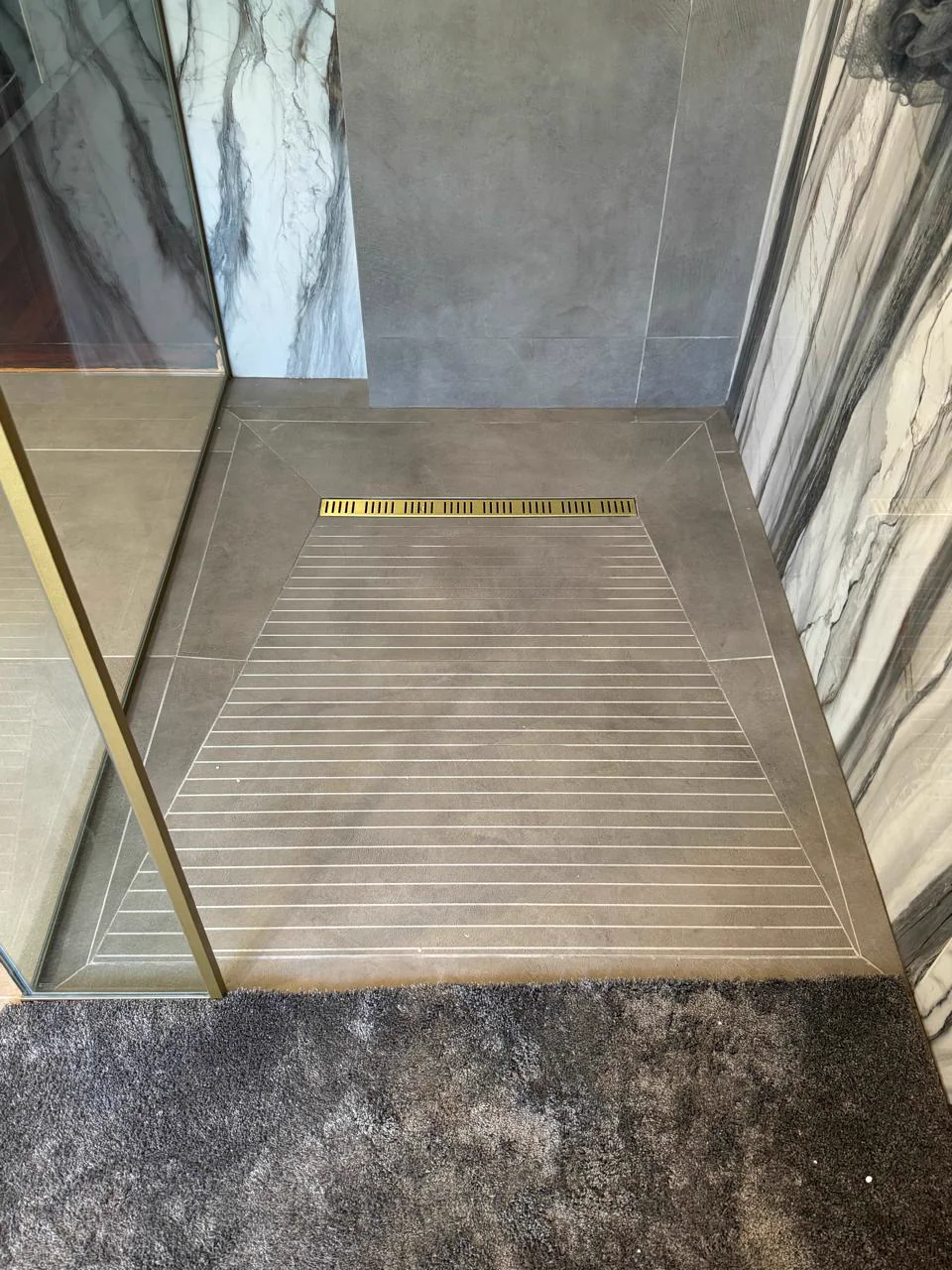 Close view of a tiled walk-in shower with frameless glass and a linear drain